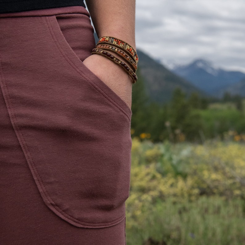 May include: A close-up of a maroon skirt with a large pocket on the left side. The skirt is made of a soft, comfortable fabric. The person wearing the skirt is wearing several bracelets on their wrist.