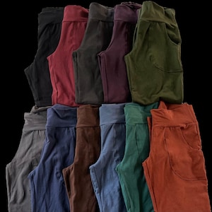 May include: A stack of 12 pairs of casual pants in various colors, including gray, navy blue, brown, burgundy, dark green, and rust.