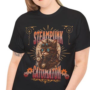 May include: A black t-shirt featuring a graphic print of a cat wearing goggles and mechanical gear. The text "STEAMPUNK" appears above the cat, and "CATOMATON" is printed below. The design includes clock faces, gears, and decorative lines.