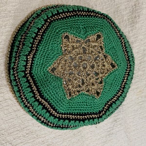 Può includere: Kippah fatta a mano, all'uncinetto, di colore verde vibrante, con un motivo a stella dorata al centro. I bordi sono rifiniti con filo dorato e nero, creando un bordo decorativo. Questo copricapo è un articolo tradizionale.