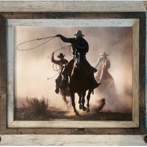 May include: Three cowboys on horseback ride through a dusty landscape. The cowboy in the foreground is throwing a lasso. The cowboys are silhouetted against a bright, hazy sky.