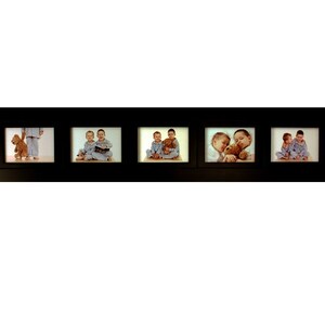 May include: A black multi-photo frame with five rectangular openings. Each opening contains a photograph of children with teddy bears. The children are wearing pajamas. The frame is horizontal and has a simple, modern design.