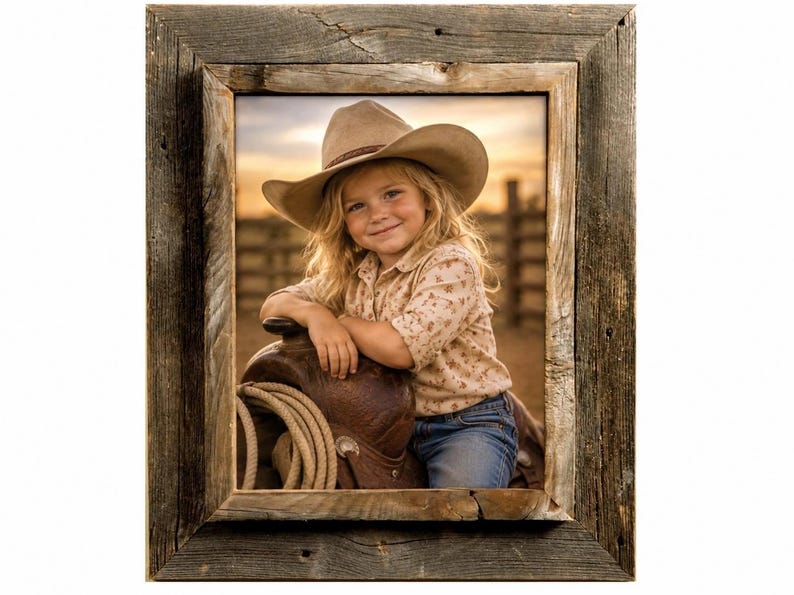 May include: A rectangular picture frame crafted from weathered, dark brown reclaimed wood with a visible grain. The frame encloses a photograph of a child wearing a tan cowboy hat and a patterned shirt, leaning on a brown leather saddle.