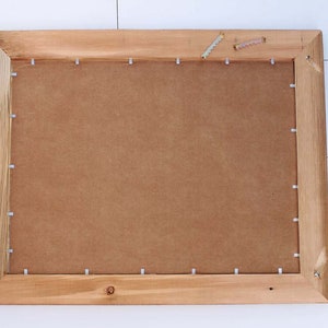 May include: The back of a wooden picture frame with a brown cardboard backing. The frame is secured with small silver staples.