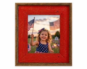 May include: A rustic wooden picture frame with a red painted interior and a natural wood-toned exterior. The frame surrounds a photograph of a young child holding an American flag and sparklers, celebrating a patriotic event.