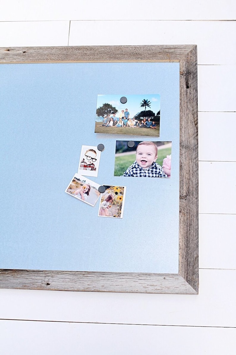 May include: A light blue magnetic board with a wood frame, holding several photos of people. The photos are held in place with small black magnets.