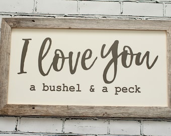 May include: A rustic wooden framed sign with a white background and brown text that reads "I love you a bushel & a peck".