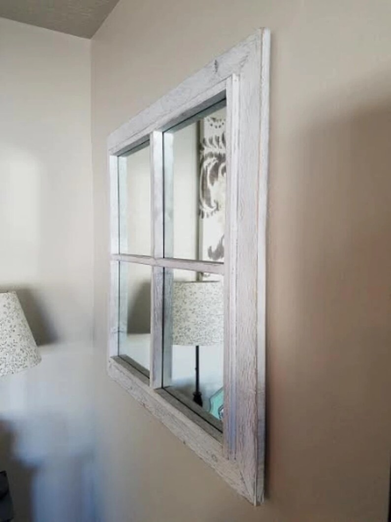 Puede incluir: Un espejo con marco de madera blanqueado con un dise&ntilde;o de ventana de cuatro paneles. El espejo est&aacute; colgado en una pared de color beige claro.