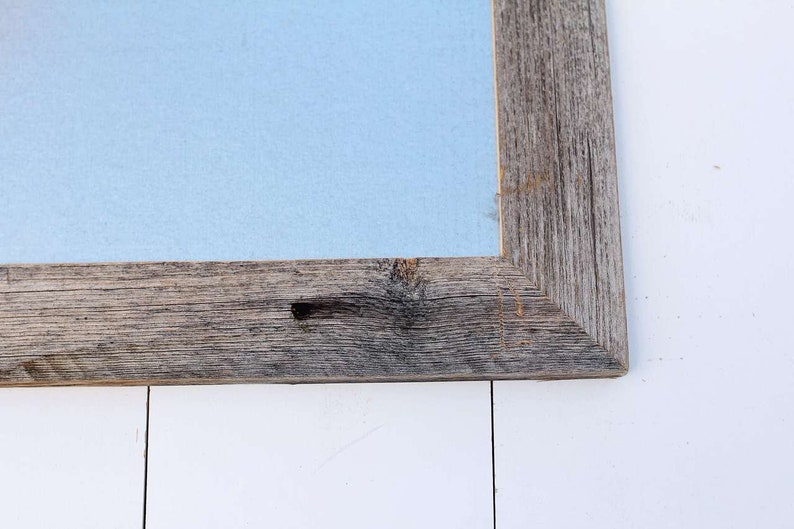 May include: Close-up of the corner of a rustic wooden frame with a light blue background. The frame is made of weathered wood with knots and grain.