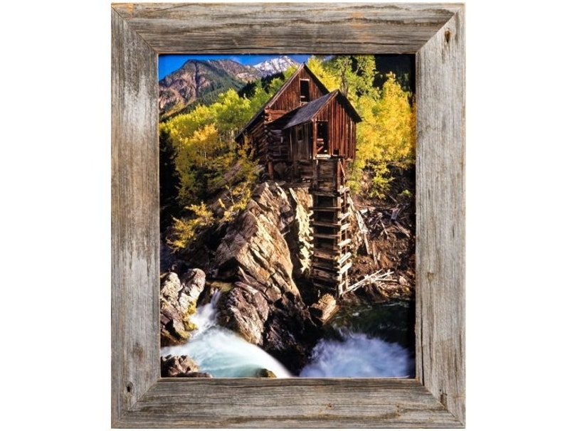 May include: A framed print of a rustic wooden mill perched on a rocky cliff, with a waterfall cascading below. The surrounding landscape features vibrant yellow and green trees, and a mountain range in the background. The frame is made of weathered wood.