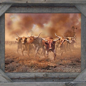 May include: A framed print of a herd of longhorn cattle running through a dusty field. The cattle are brown and white with long horns. The sky is a dusty orange color. The frame is made of rustic wood with barbed wire accents.