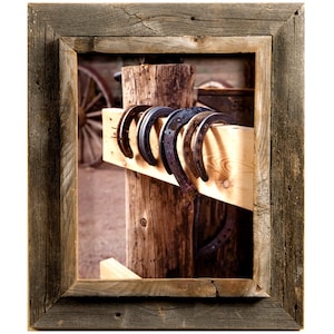 May include: A rustic wooden frame with a picture of a wooden post with several rusty horseshoes hanging on it.