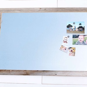 May include: A light blue magnetic board with a rustic wood frame. The board has several photos attached with magnets.