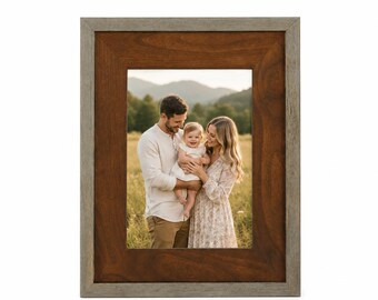 May include: Rectangular wooden picture frame with a two-tone design. The inner frame is a warm brown, while the outer frame has a gray-green finish. The frame holds a family portrait of a couple and a baby in a field.