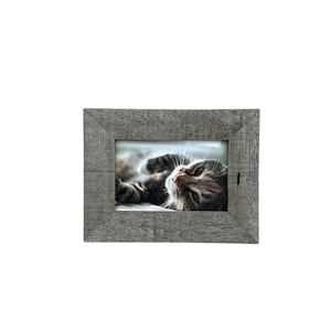 May include: A rectangular, gray wooden picture frame with a photo of a cat. The cat is lying down and looking up. The frame has a rustic, weathered appearance, with visible wood grain.