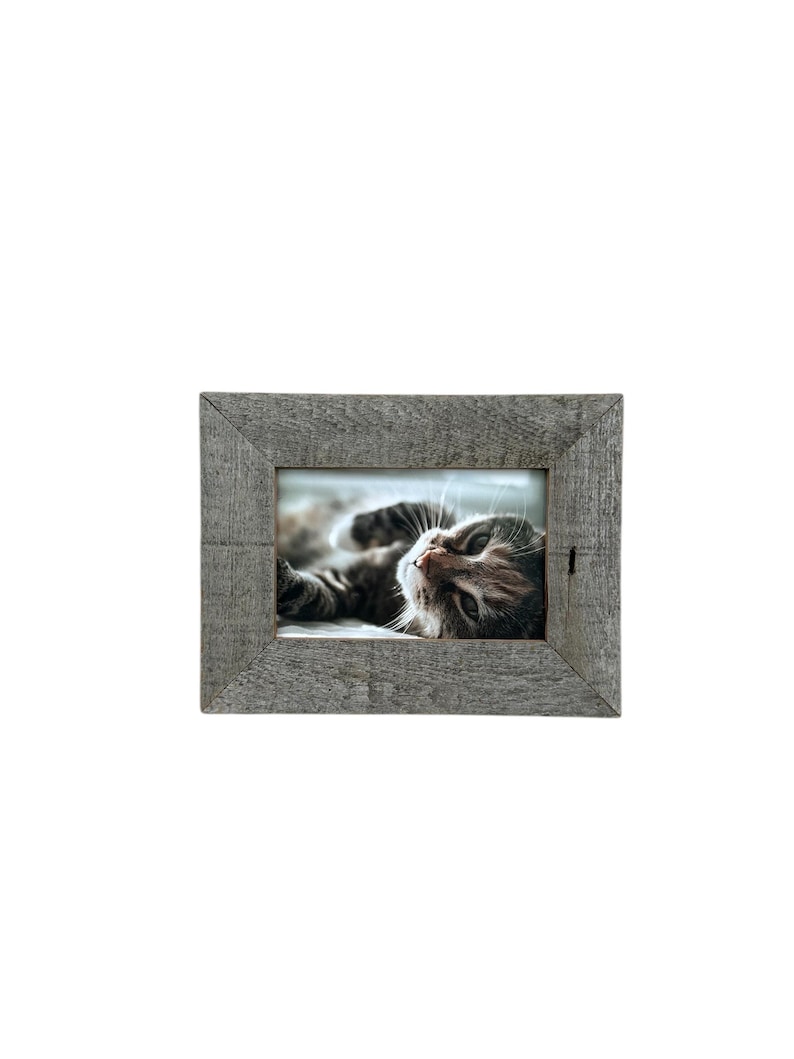 May include: A rectangular, gray wooden picture frame with a photo of a cat. The cat is lying down and looking up. The frame has a rustic, weathered appearance, with visible wood grain.