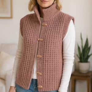 Può includere: Un gilet lavorato a maglia rosa polveroso con collo alto e bottoni in legno. Il gilet senza maniche presenta una trama a coste ed è indossato sopra una camicia bianca a maniche lunghe e jeans blu. Il gilet è un capo a strati comodo ed elegante.