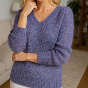 Könnte beinhalten: Ein periwinkelfarbener V-Ausschnitt-Pullover mit zartem Lochmuster. Das langärmelige Strickteil hat eine weiche, flauschige Textur. Das Model trägt eine goldene Halskette. Der Pullover ist ein bequemes und stilvolles Kleidungsstück für kühlere Tage.