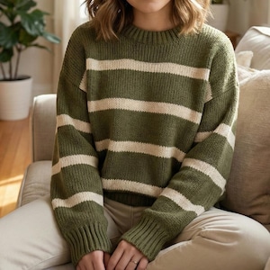 Könnte beinhalten: Olivgrüner und cremefarbener gestreifter Pullover. Der Pullover hat einen Rundhalsausschnitt und lange Ärmel. Der dicke Strick ist ein lässiger Stil. Die horizontalen Streifen sind gleichmäßig über Körper und Ärmel verteilt. Der Pullover ist eine bequeme Alltagskleidung.