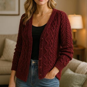 Könnte beinhalten: Burgunderfarbene Strickjacke mit Zopfmuster, V-Ausschnitt und Knopfverschluss. Der langärmlige Pullover wird mit einer blauen Jeans kombiniert. Die Frau trägt ein schwarzes Top und eine goldene Halskette.
