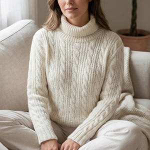 May include: Cream-colored cable knit turtleneck sweater. The sweater features a classic cable knit design with a ribbed turtleneck and cuffs. The long-sleeved sweater is made of a soft, warm material, perfect for cooler weather.