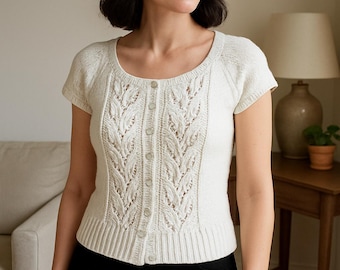 May include: Cream-colored short-sleeve cardigan with a button-up front and a round neckline. The knitwear features a detailed leaf pattern down the center. The model is wearing black pants.
