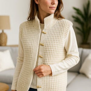 Pu&ograve; includere: Gilet in maglia color crema con collo alto e chiusure a toggle in legno. La maglia strutturata &egrave; indossata sopra una camicia color crema a maniche lunghe e abbinata a jeans blu. Il gilet presenta un motivo a coste verticali.