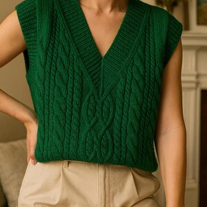 Puede incluir: Un chaleco verde de punto trenzado con cuello en V profundo. La parte superior sin mangas presenta un patr&oacute;n texturizado y se combina con pantalones beige. El estilo general sugiere una est&eacute;tica cl&aacute;sica y preppy, adecuada para combinar capas.