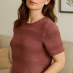 Puede incluir: Una camiseta de punto rojo ladrillo de manga corta, con cuello redondo y patrón de chevrón texturizado. La parte superior está hecha de un material de punto suave. Las mangas son cortas y el ajuste es relajado.