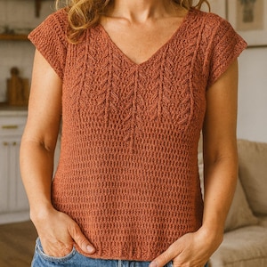 May include: A rust-colored, short-sleeved top with a V-neck. The top features a textured knit pattern with vertical leaf-like designs down the front. The model is wearing blue jeans.