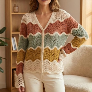 Puede incluir: Un cárdigan calado multicolor con cuello en V y cierre de botones. El suéter presenta bandas horizontales en crema, óxido, verde, amarillo y marrón. Las mangas y el dobladillo tienen un borde festoneado. El cárdigan se lleva sobre pantalones color crema.