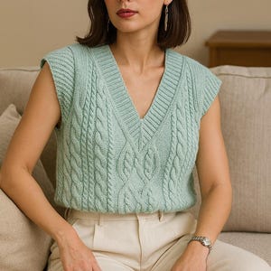 Puede incluir: Un chaleco de punto verde claro con cuello en V y dise&ntilde;o de punto trenzado. La parte superior sin mangas se usa con pantalones color crema. El chaleco es de un color verde suave y apagado. La modelo lleva un reloj plateado.