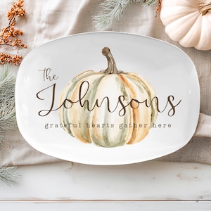 May include: White oval serving platter with a watercolor pumpkin design. The platter has the text "The Johnsons" and "grateful hearts gather here" in a script font. The pumpkin is in shades of green, orange, and cream.