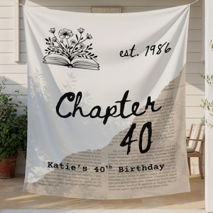 May include: A white fabric wall hanging featuring a black line drawing of an open book with flowers emerging from the pages. The text reads est. 1986, Chapter 40, and Katie's 40th Birthday, overlaid on a background of printed Latin text.