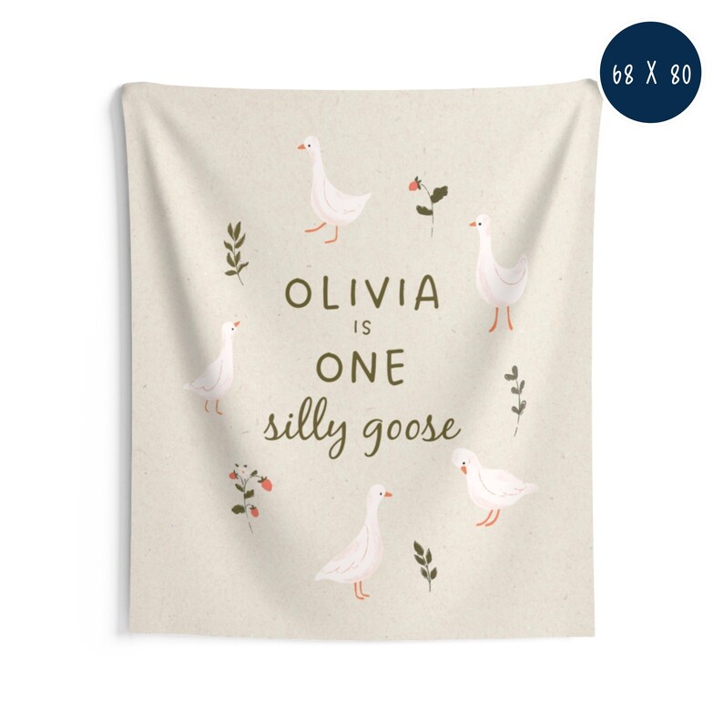 May include: A beige wall tapestry with the text "OLIVIA is ONE silly goose" in brown. The tapestry features illustrations of white geese, red berries, and green leaves. Dimensions are 68 x 80 inches.