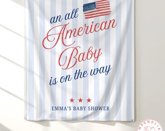 May include: A rectangular fabric wall hanging featuring vertical light blue and white stripes. The text reads an all American Baby is on the way in red and blue script and print, with a small American flag graphic and EMMA'S BABY SHOWER.