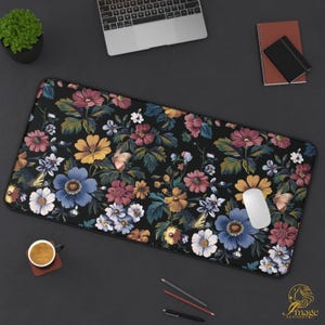 Puede incluir: Alfombrilla de escritorio negra con un vibrante estampado floral. Presenta flores azules, amarillas, rosas y blancas. La alfombrilla rectangular está diseñada para ratón y teclado, mide unos 80 cm de largo.