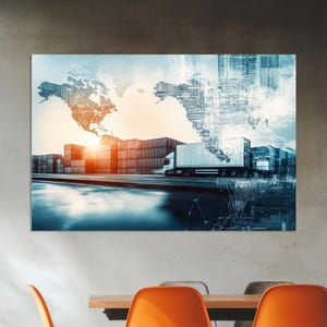 May include: A digital art print depicting global shipping and logistics. The image features a world map overlayed on a scene of shipping containers, a semi-truck, and a sunrise. The print is displayed on a wall above a table and orange chairs.