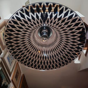May include: A large, circular pendant light fixture with a black and white geometric pattern. The light has a chrome finish and a single exposed light bulb. The fixture is hanging from the ceiling.