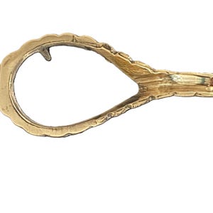 May include: A vintage gold-toned tie clip with a unique, openwork design. The clip features a textured, ridged section on one end and a decorative, scalloped edge along the open loop. The overall shape is elongated and asymmetrical.