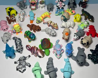 May include: A collection of colorful, segmented, articulated animal figurines. The figurines are made of plastic and feature a variety of animals, including a bee, a koala, a turtle, a dolphin, a raccoon, a cat, a mouse, a panda, a seal, a lizard, a snake, a cow, a gorilla, a bat, a dinosaur, a platypus, a skunk, a worm, and an elephant.