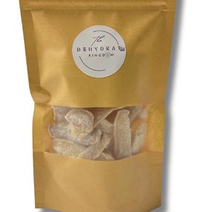 May include: A kraft paper bag with a clear window, filled with dehydrated fruit. The bag has a white circular label with the text "The DEHYDRATED KINGDOM" in a stylized font. The dried fruit pieces are light in color.