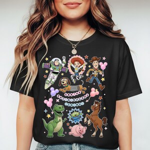 May include: Black t-shirt featuring colorful cartoon characters from the Toy Story movie. The design includes Buzz Lightyear, Woody, Jessie, Rex, Slinky Dog, and other characters. The text "You've Got a Friend in Me" is also included.