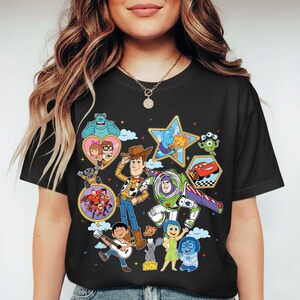 May include: Black t-shirt featuring a colorful collage of animated characters. The design includes Woody, Buzz Lightyear, Mike Wazowski, and other characters from popular animated movies. The shirt is a crew neck style.