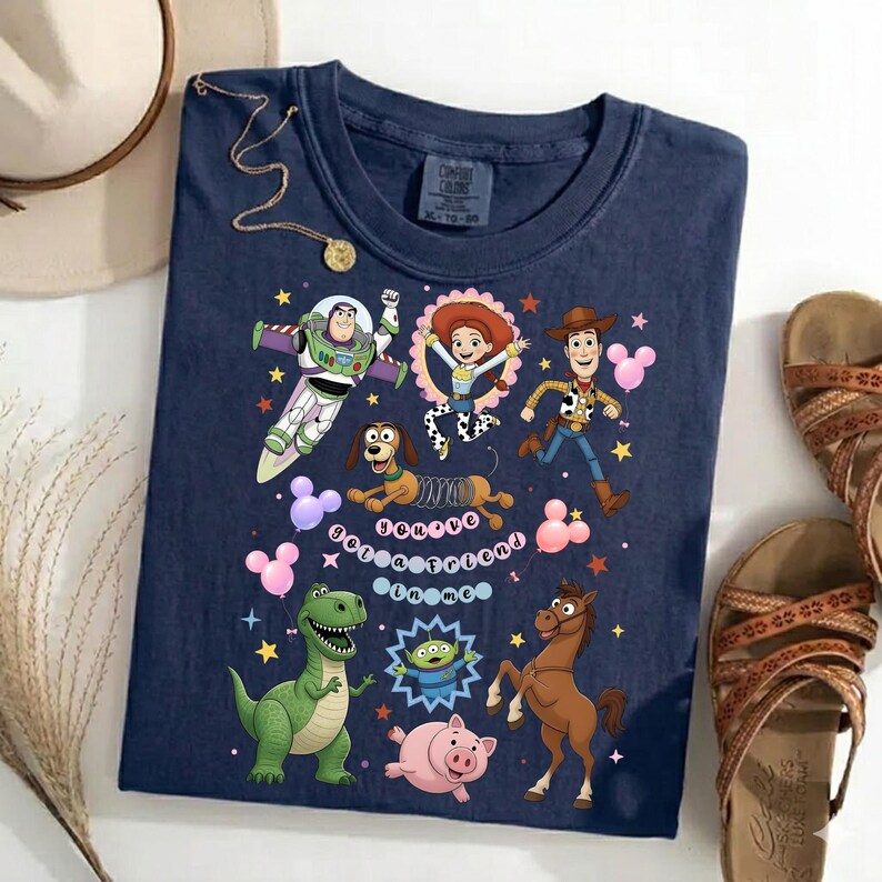 May include: Navy blue t-shirt featuring a colorful graphic of characters from the animated movie Toy Story. The design includes Buzz Lightyear, Jessie, Woody, and other characters, with the phrase "You've Got a Friend in Me".