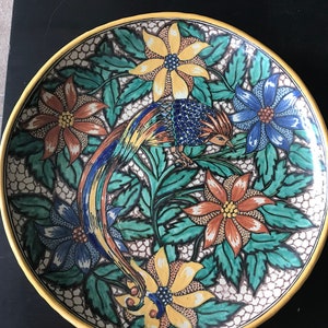Puede incluir: Un plato grande de cerámica ovalado con un diseño colorido. El plato presenta un pájaro estilizado con una cola larga, rodeado de flores y hojas. Los colores son brillantes y vibrantes, incluyendo amarillo, azul, verde, naranja y rojo.