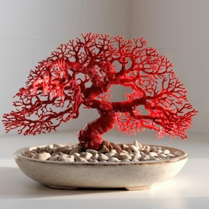 May include: A vibrant red bonsai tree sculpture. The tree features a twisted trunk and intricate branches, set in a cream-colored ceramic pot filled with small, white stones. The bonsai is a decorative piece.