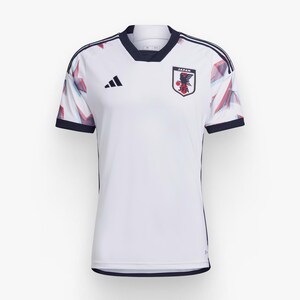 Op de afbeelding: Wit voetbaltenue met blauwe en rode accenten. Het tenue heeft een geometrisch patroon en bevat het Adidas-logo en het embleem van het Japanse nationale team met de tekst "JAPAN" en "JFA".