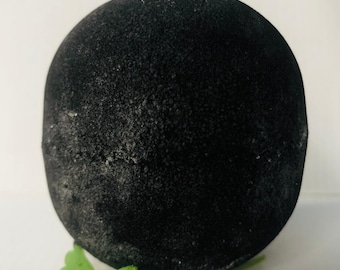 Puede incluir: Una bola de jabón de carbón negro con una textura rugosa, sentada sobre una hoja verde.