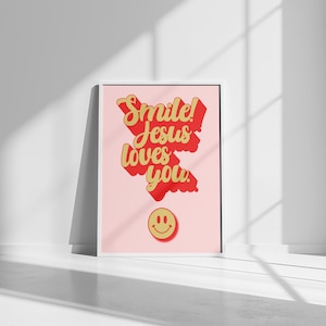 Può includere: Un poster incorniciato rosa e bianco con il testo "Smile! Jesus loves you." in lettere rosse e dorate. Un'emoticon gialla sorridente si trova nella parte inferiore del poster.